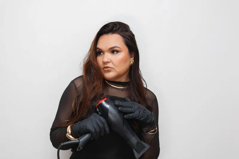Portrait of a woman in a salon holding a hair dryer, wearing elegant gloves and jewelry