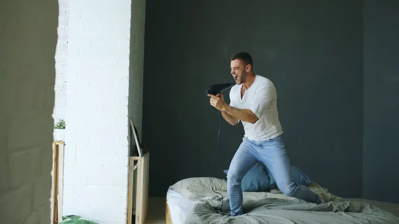 Joyful man singing with a hair dryer in a stylish modern bedroom