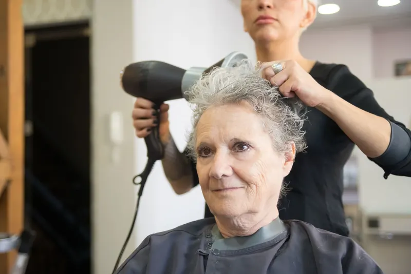 Elderly woman with white hair receiving a blow-dry at a hair salon in Portugal