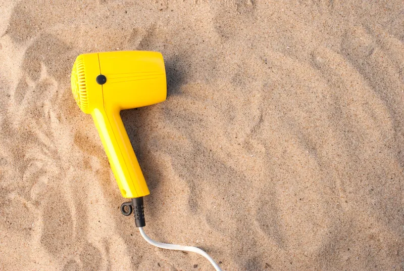 A yellow hair dryer resting on smooth sand, captured in a high angle shot