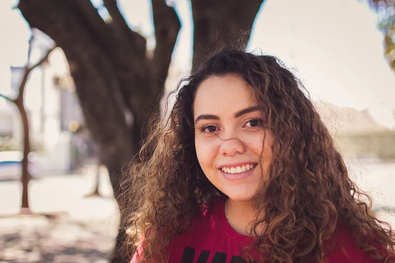 Portrait of a smiling young woman with curly hair in a sunny outdoor setting